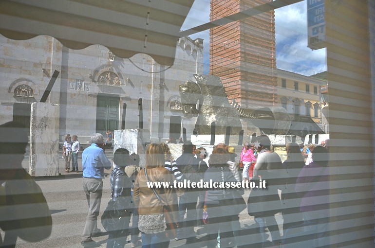 PIETRASANTA (Piazza Duomo) - Alcuni visitatori della mostra di Gustavo Aceves (Lapidarium work in progress) riflessi in una vetrina. Sullo sfondo la scultura monumentale "Cavallo di Troia"